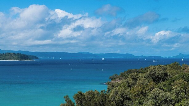 Un paisaje costero con cielo despejado, mar tranquilo y montañas al distante.