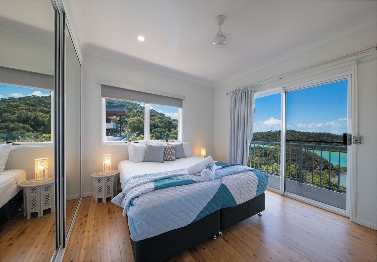 A bedroom with a bed, bedside tables, a window, and a balcony with a view.