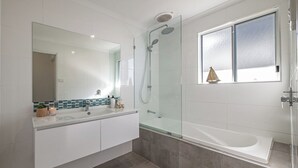Un baño moderno con ducha envuelta en vidrio, un espejo grande y una bañera.
