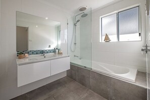 A modern bathroom with a glass-enclosed shower, a large mirror, and a bathtub.