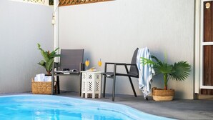 Zona de piscina amb una cadira relaxant, una taula petita amb begudes i plantes en testos.