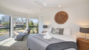 Quarto de hotel moderno com uma cama grande, um ventilador de teto, vista para a cidade e varanda com uma cadeira.