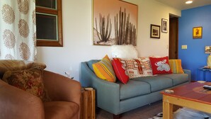 En stue med sofa, sofabord og et mønstret gardin.