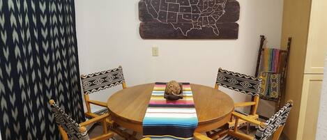 Een ronde houten eettafel met een kleurrijke strepen tafelkleed, omringd door vier stoelen met gestreepte kussens. Er staat een decoratief object op de tafel.