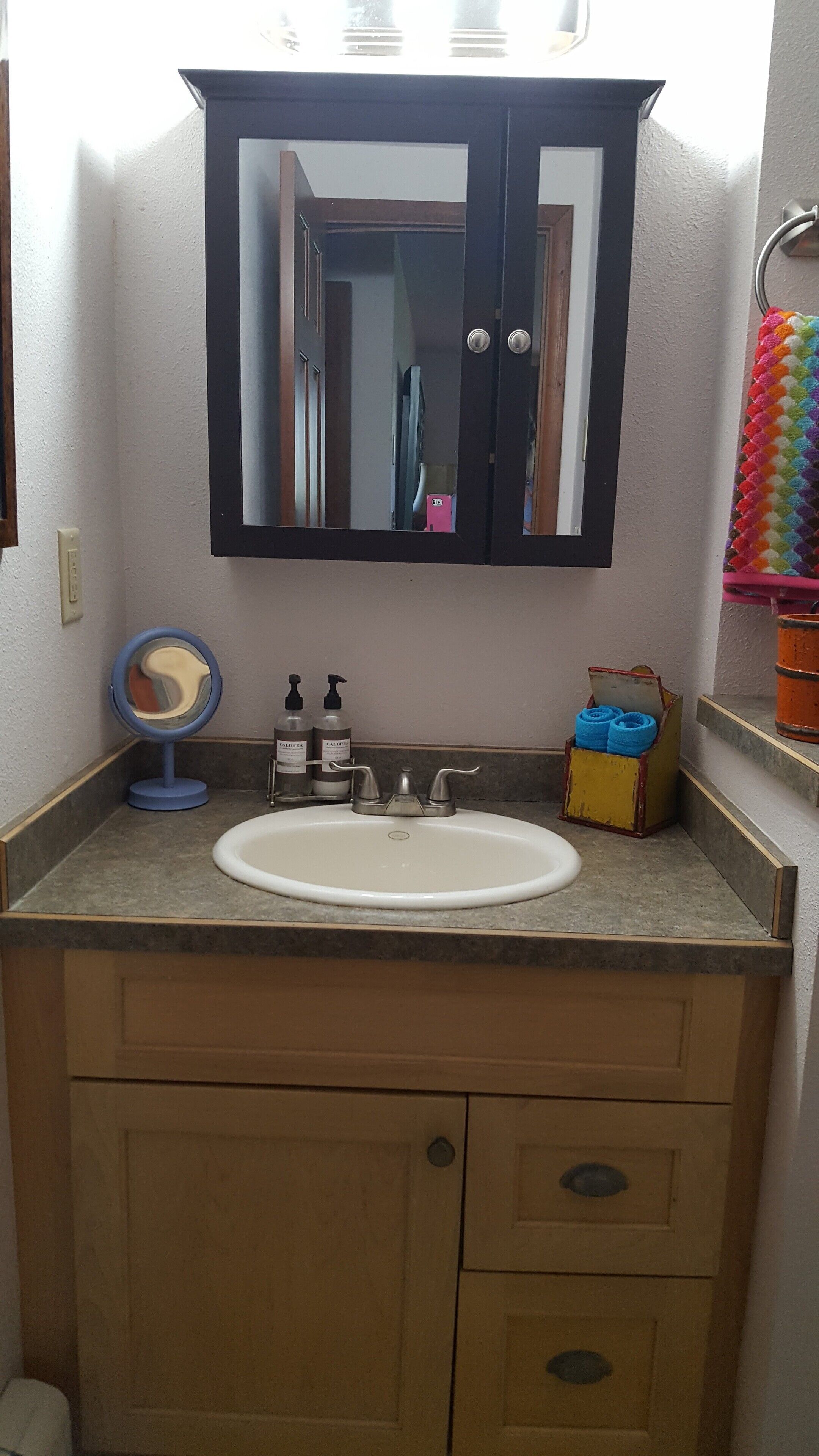 A bathroom with a white sink, a mirror above it, and a wooden cabinet below. There are two bottles of lotion on the counter.