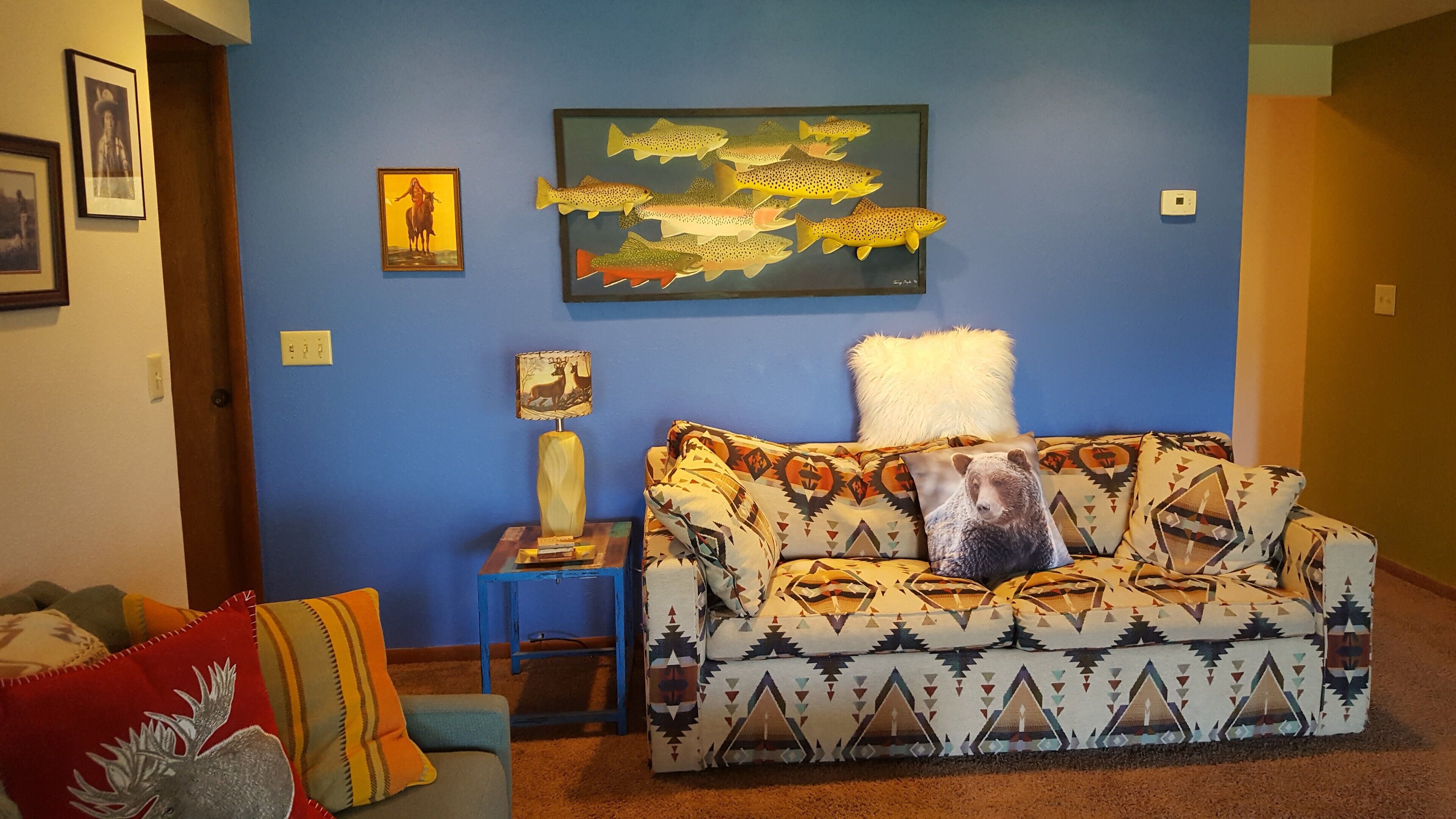 A living room with a blue wall, a patterned sofa, a decorative lamp, and framed artwork.