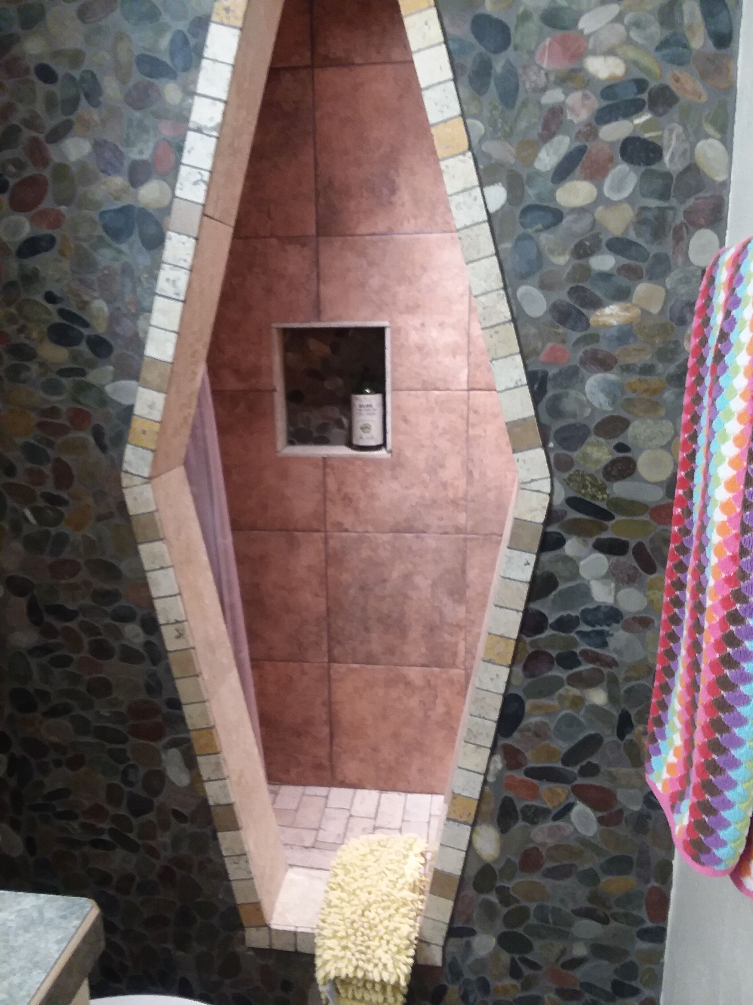 A bathroom with a pebble-patterned wall, a tiled floor, and a small shelf with a bottle.