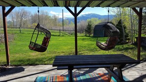 A covered patio with a wooden table and two wicker swings. - Black Bear Inn,Bridger views, E. Gallatin river access via cherry creek ponds. (Bozeman)