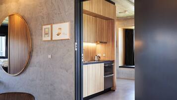 Eine moderne Küche mit Holzschränken, einer Edelstahlspüle und einem Wasserkocher. An der Wand hängt ein gerahmtes Bild und links befindet sich ein Spiegel.
