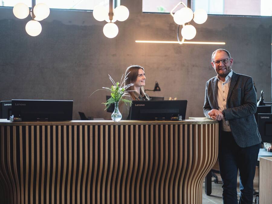 A reception desk with Lenovo computers, a vase with greenery, and a modern, curved design.