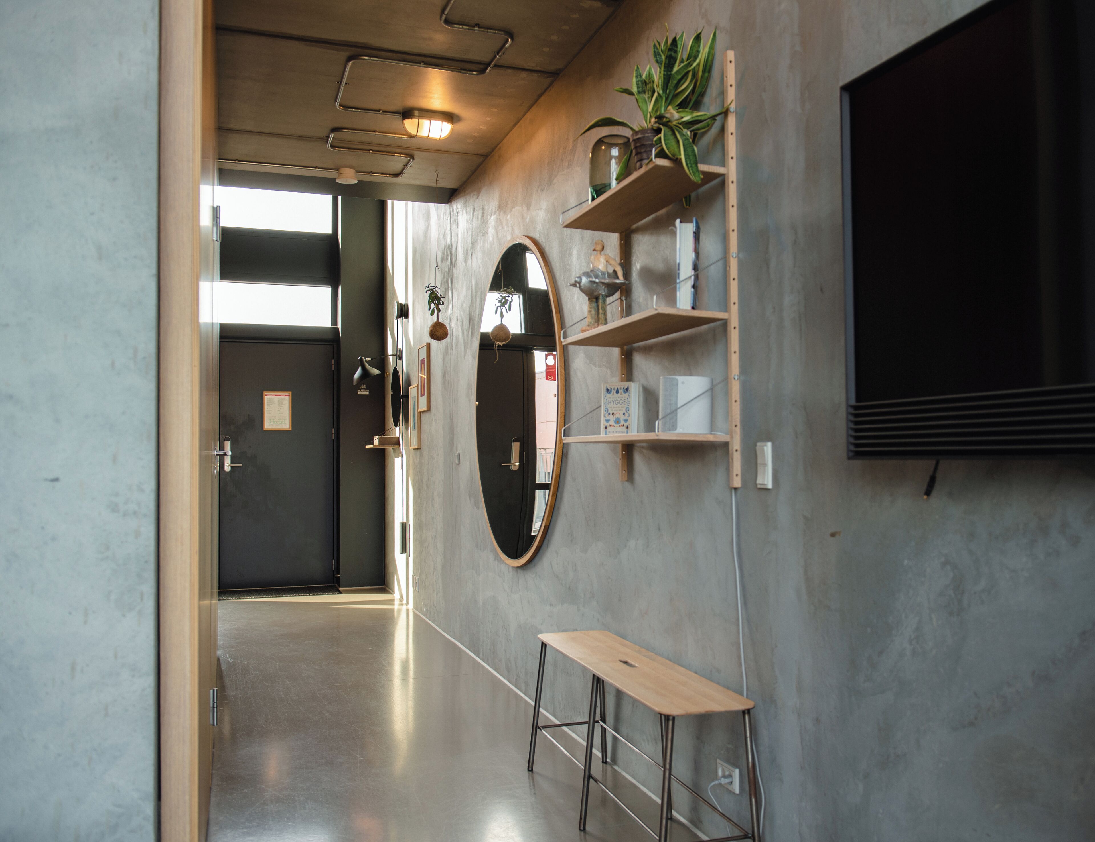 A hallway with a wooden bench, a large mirror, and shelves with plants and books.