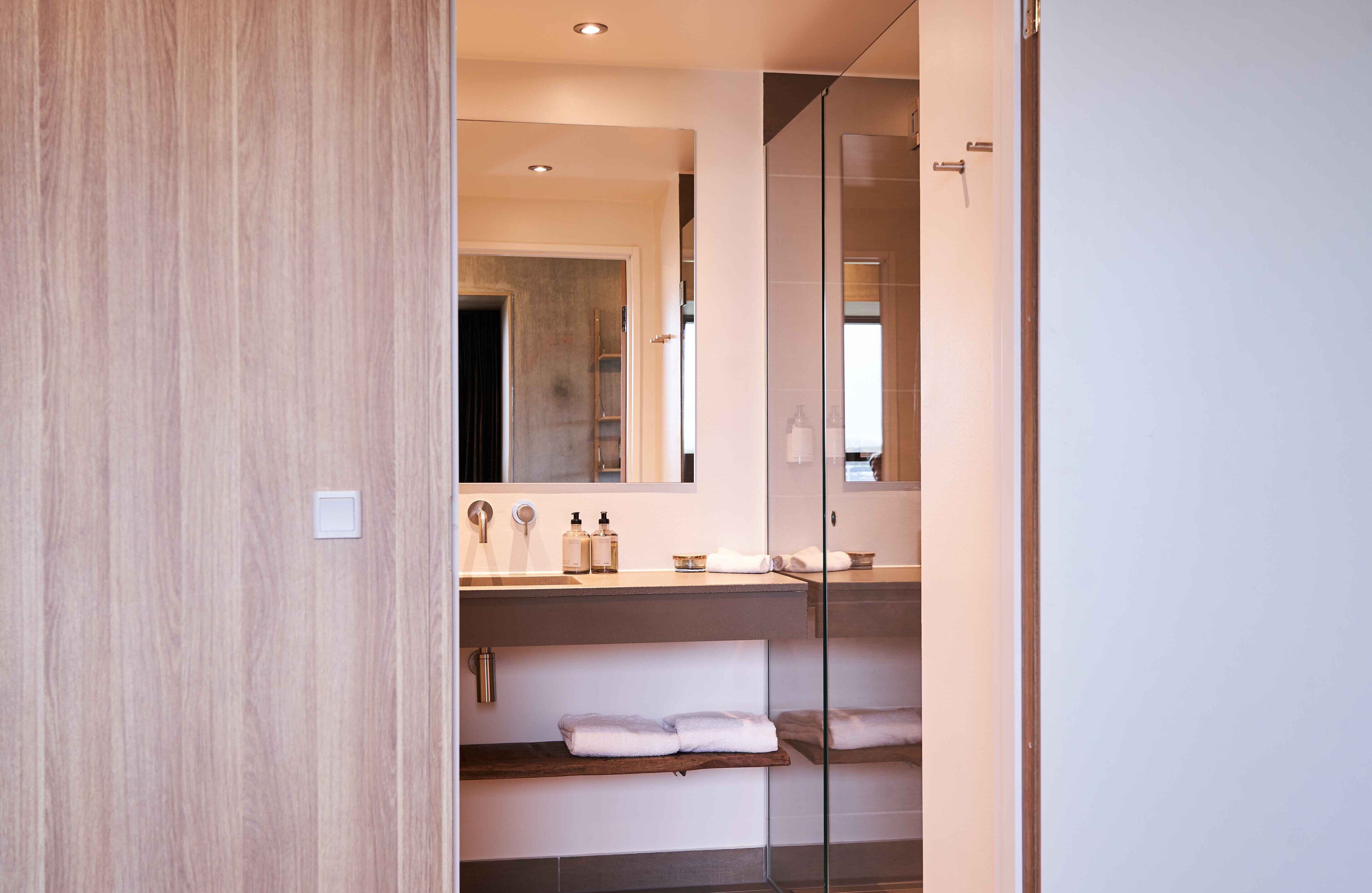 A modern bathroom with a wooden vanity, a glass shower enclosure, and a large mirror.