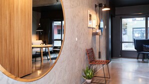 Un interior moderno con un separador de madera, un espejo redondo, una planta en maceta y una zona de estar con una silla y una mesa.