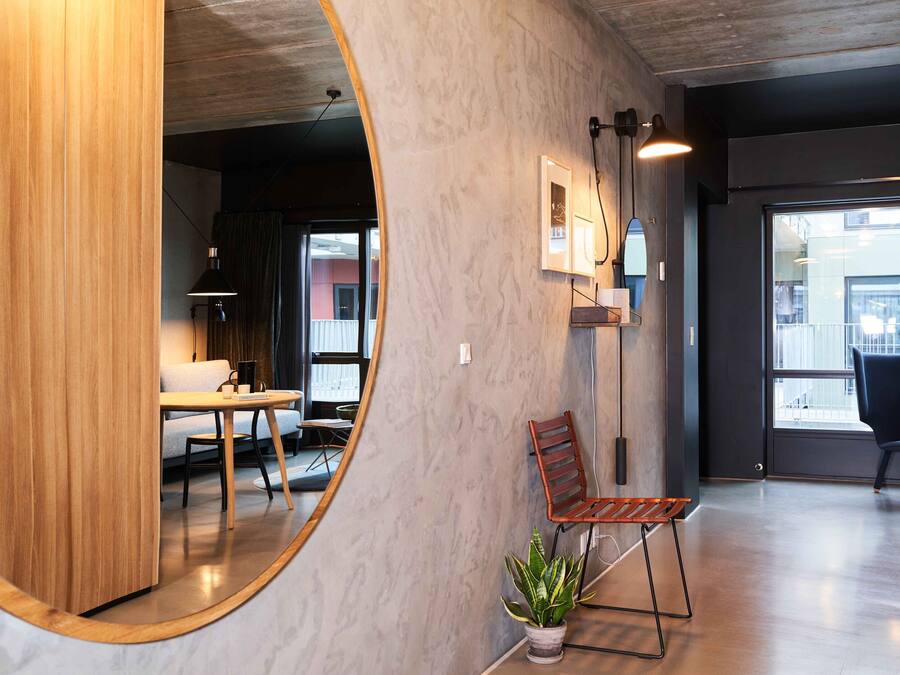 A modern interior with a wooden partition, a round mirror, a potted plant, and a seating area with a chair and table.