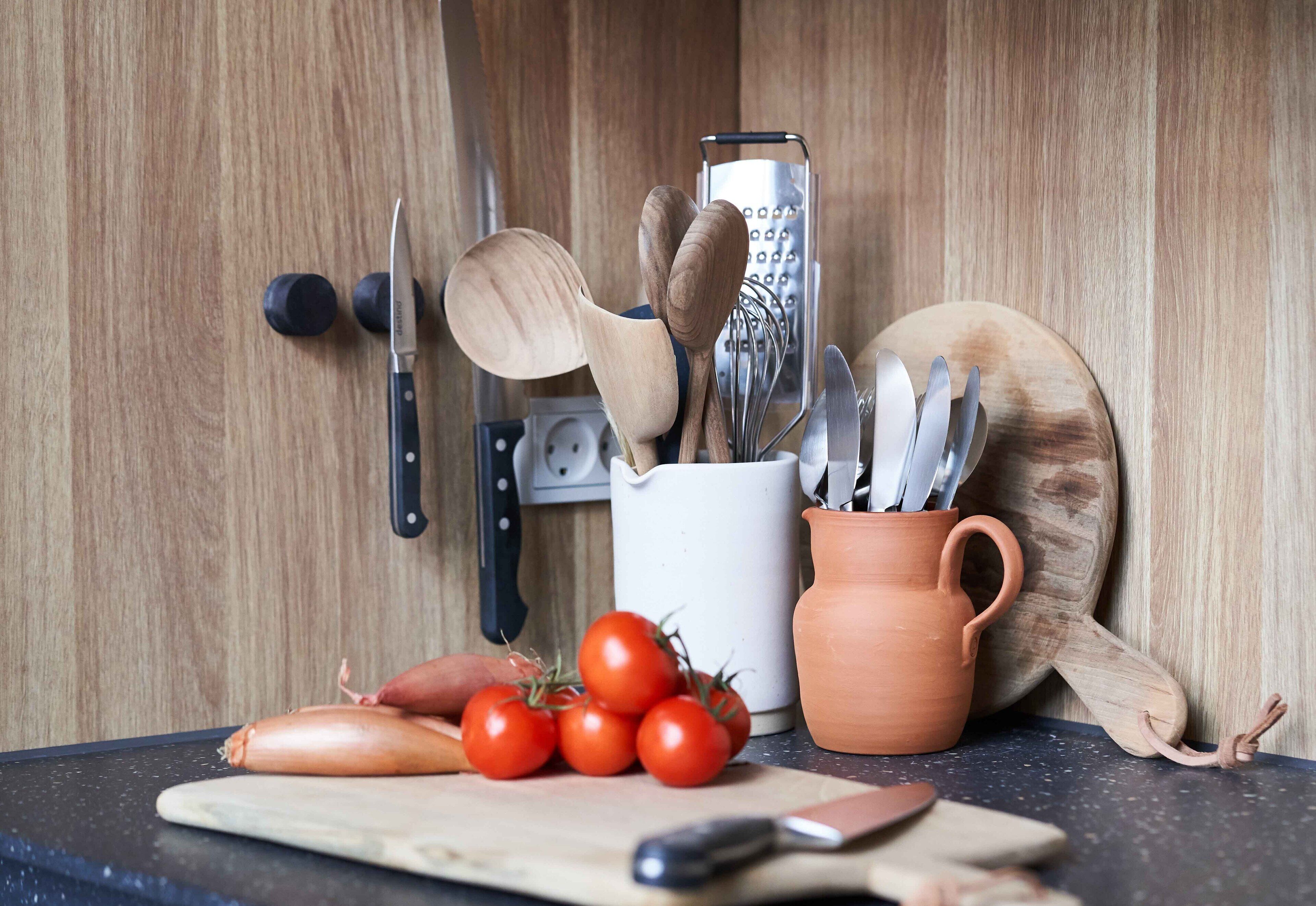 Un plan de travail de cuisine avec une planche à découper, un couteau, une tomate et une cuillère en bois.