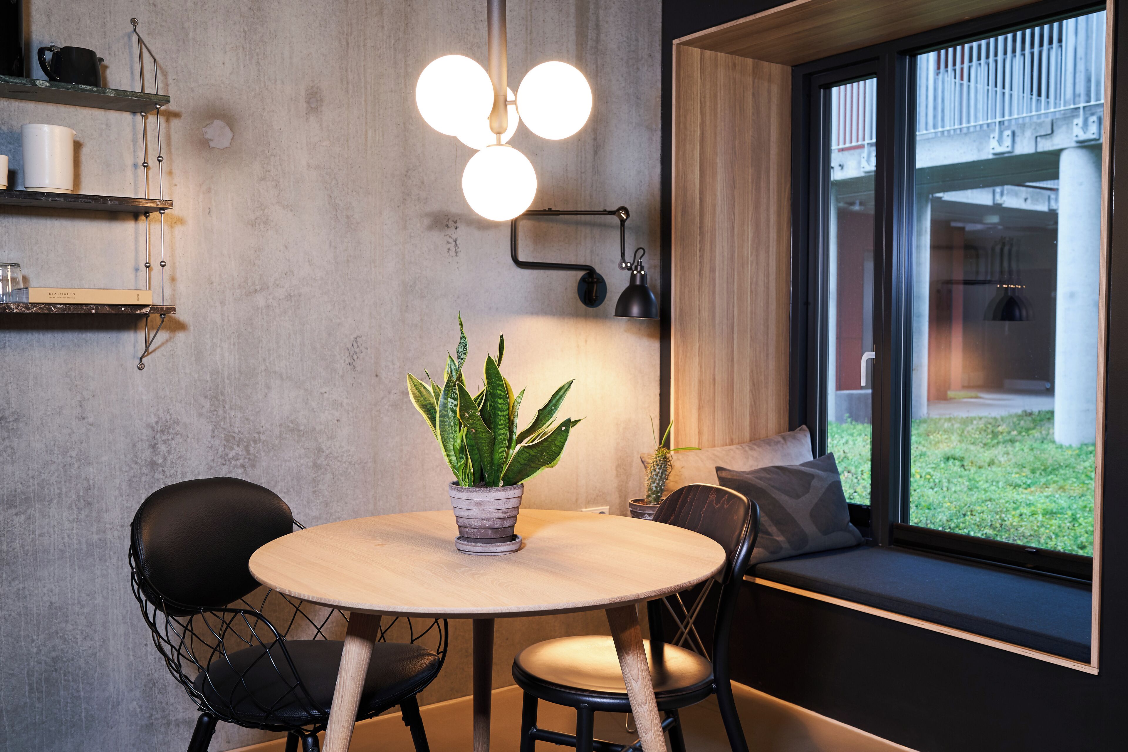 A modern dining area with a round table, two chairs, a potted plant, and a window with a view of the outside.