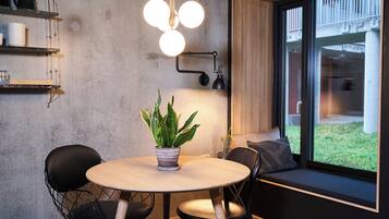 A modern dining area with a round table, two chairs, a potted plant, and a window with a view of the outside.