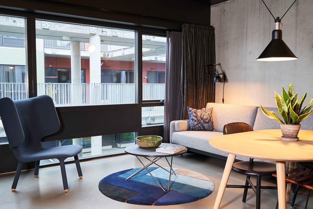 A modern living room with a sofa, a dining table, a chair, a potted plant, and a view of an outdoor balcony.