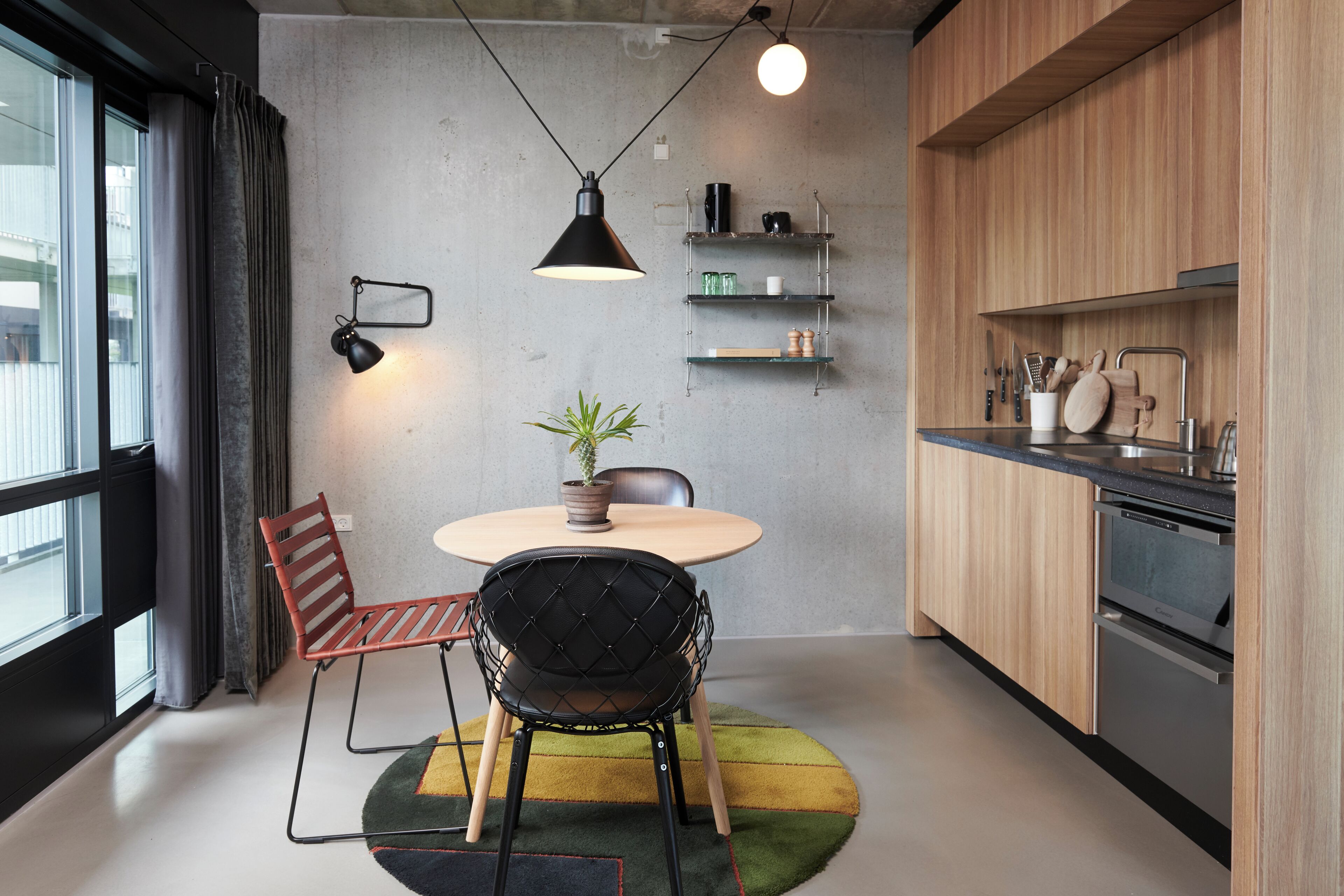 A modern kitchen with a round table, two chairs, a potted plant, and built-in appliances.