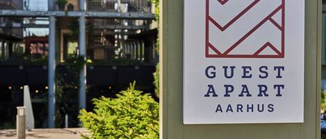 A sign for 'Guest Apart Aarhus' with a chevron logo, indicating a reception and lounge/café area.
