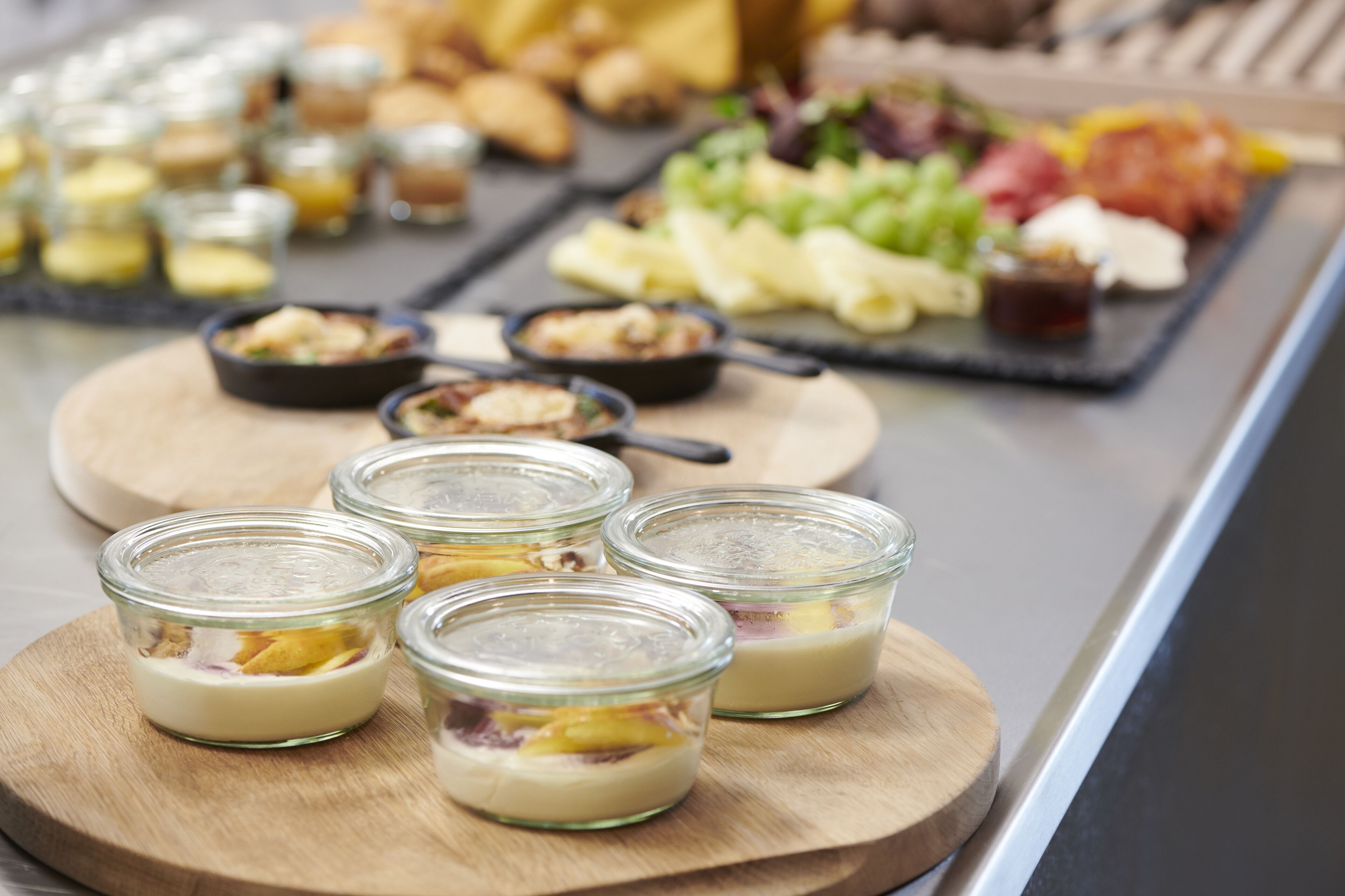 A buffet with various food items including small glass containers of dessert, a selection of fruits, and other dishes.