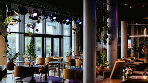 A modern restaurant with large windows, yellow chairs, and hanging plants. - Hotel GUESTapart (Aarhus)