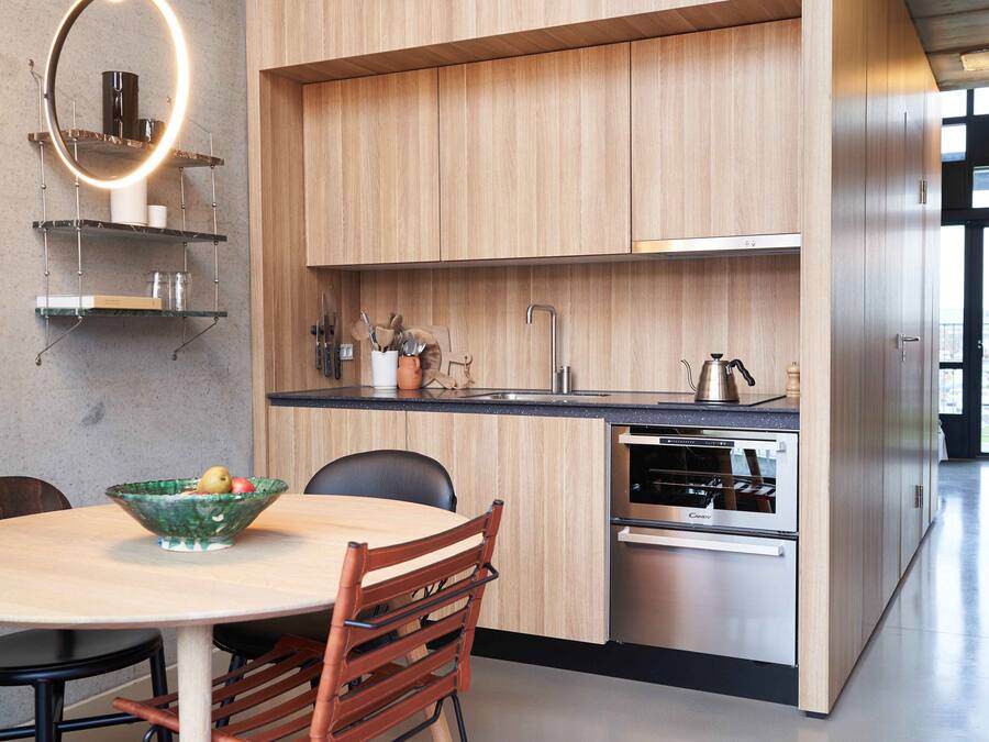 Una cocina moderna con armarios de madera, horno empotrado y comedor con una mesa redonda y sillas.
