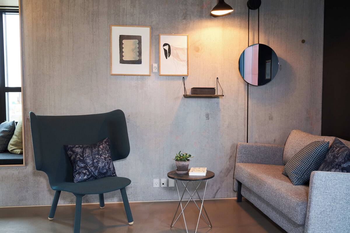A modern living room with a dark blue armchair, a grey sofa, and a small round table with a plant and a book.