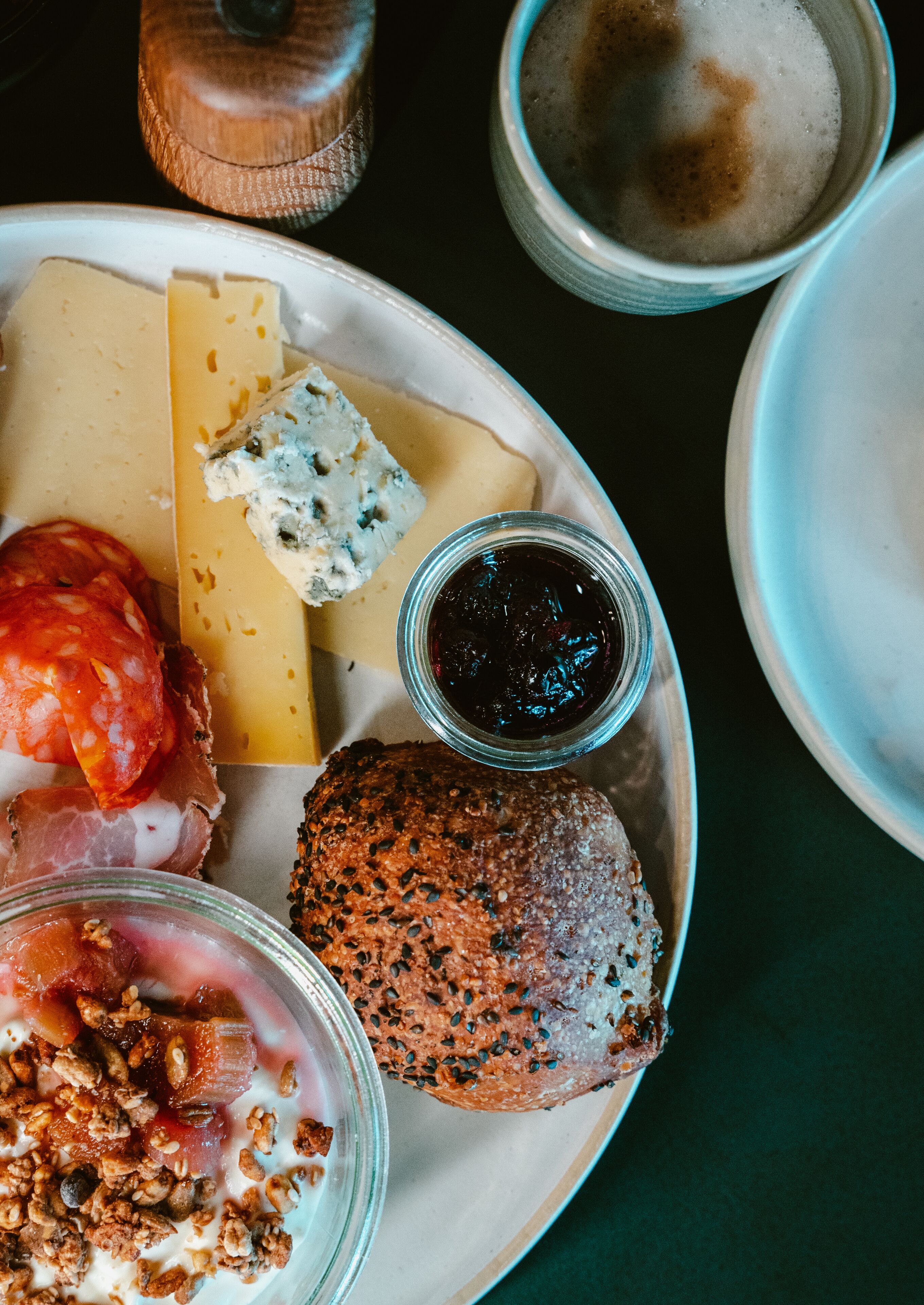 A plate with various cheeses, a croissant, and a bowl of granola.