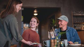 Un grupo de personas sentadas alrededor de una mesa, con un menú, una cafetera y un jarrón con una planta.