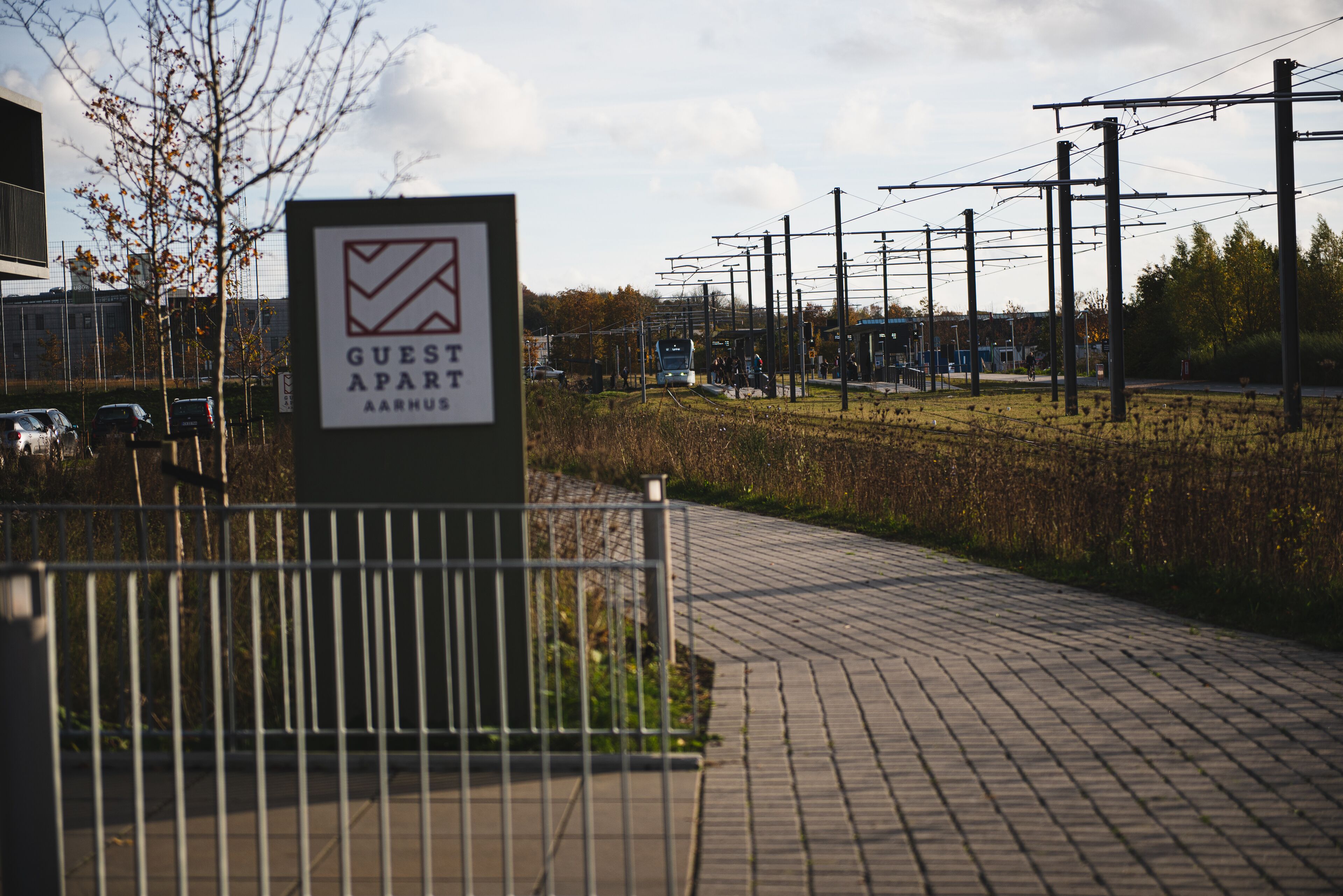 Skilt til et gæsteværelse med et ternet logo, en belagt sti og et hegn.