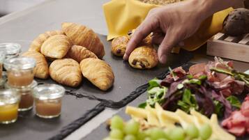 A table with croissants, grapes, cheese, and a hand reaching for a pastry.