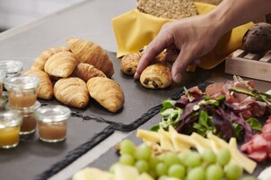A table with croissants, grapes, cheese, and a hand reaching for a pastry.