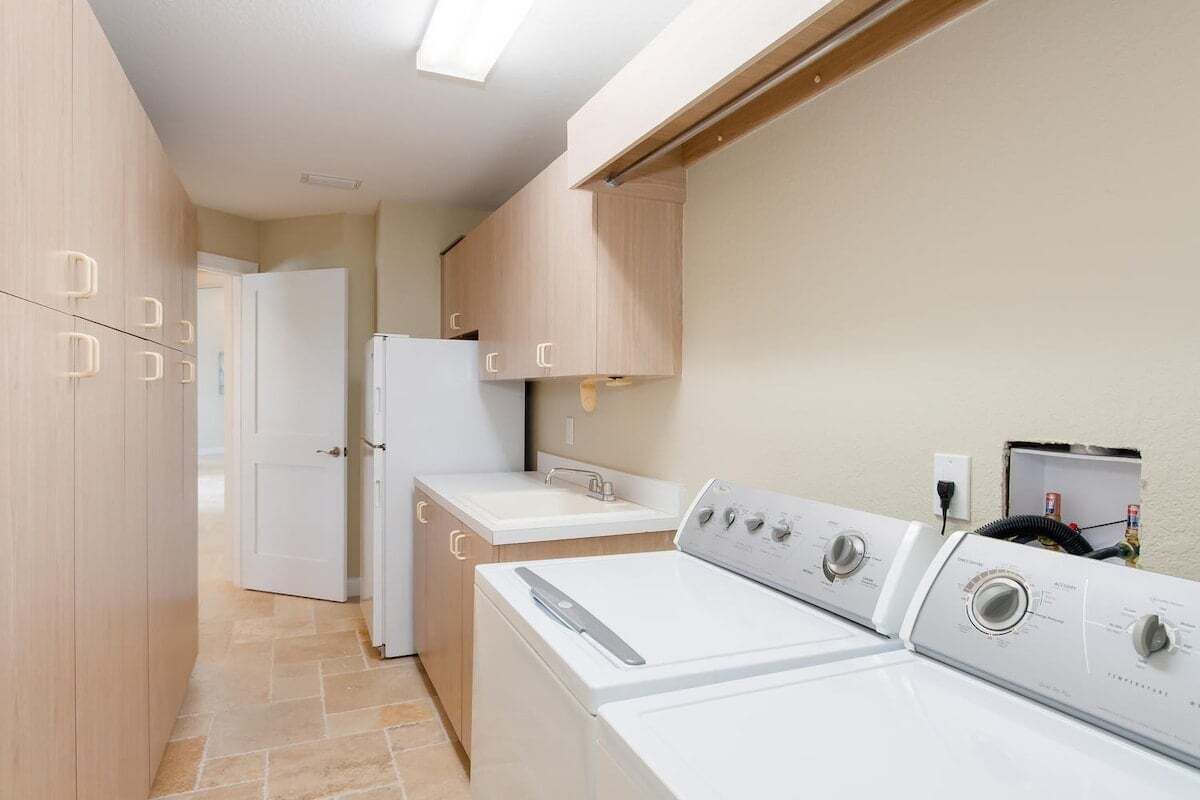 A laundry room with two washing machines, a sink, and wooden cabinets.