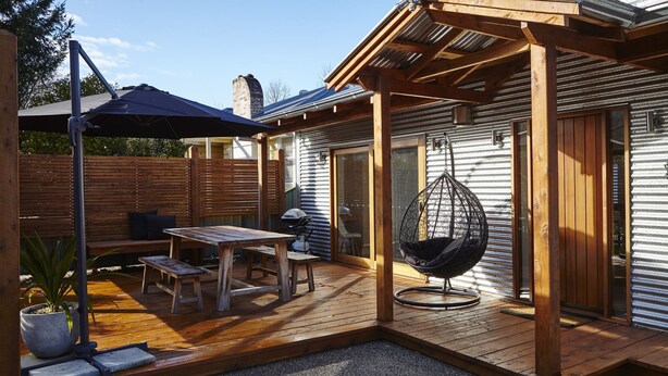 Una terraza de madera con una mesa, sillas y una mecedora, además de una planta en maceta.