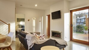 Una sala de estar moderna con chimenea, un sofá, un televisor y un comedor con una mesa de madera y sillas.