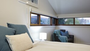 Un dormitorio con cama, una silla, una lámpara y ventana con vistas al exterior.