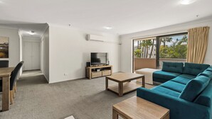 Ein modernes Wohnzimmer mit Sofa, Couchtisch, Fernseher und einem Balkon mit Vorhängen.