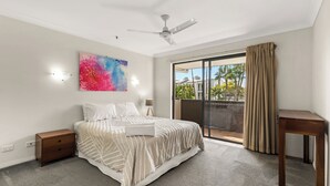 Ein Schlafzimmer mit Bett, Nachttischen, Deckenventilator, großem Fenster mit Vorhängen und einem Gemälde an der Wand.