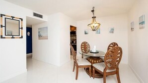 Un comedor con una mesa redonda, cuatro sillas de madera, una araña y cuadros en la pared.