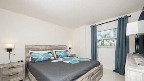 Un dormitorio con cama, mesitas de noche, cómoda y ventana con cortinas.