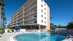 Un hotel con piscina, varios pisos y una zona cubierta con sillones de descanso.