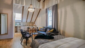 A cozy bedroom with a large bed, a dining area, a kitchen, and a window with curtains. - Peacock Boutique Apartments (Zagreb)