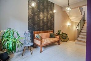 Cozy living area with a sofa, potted plant, and decorative item, featuring a staircase and warm lighting.