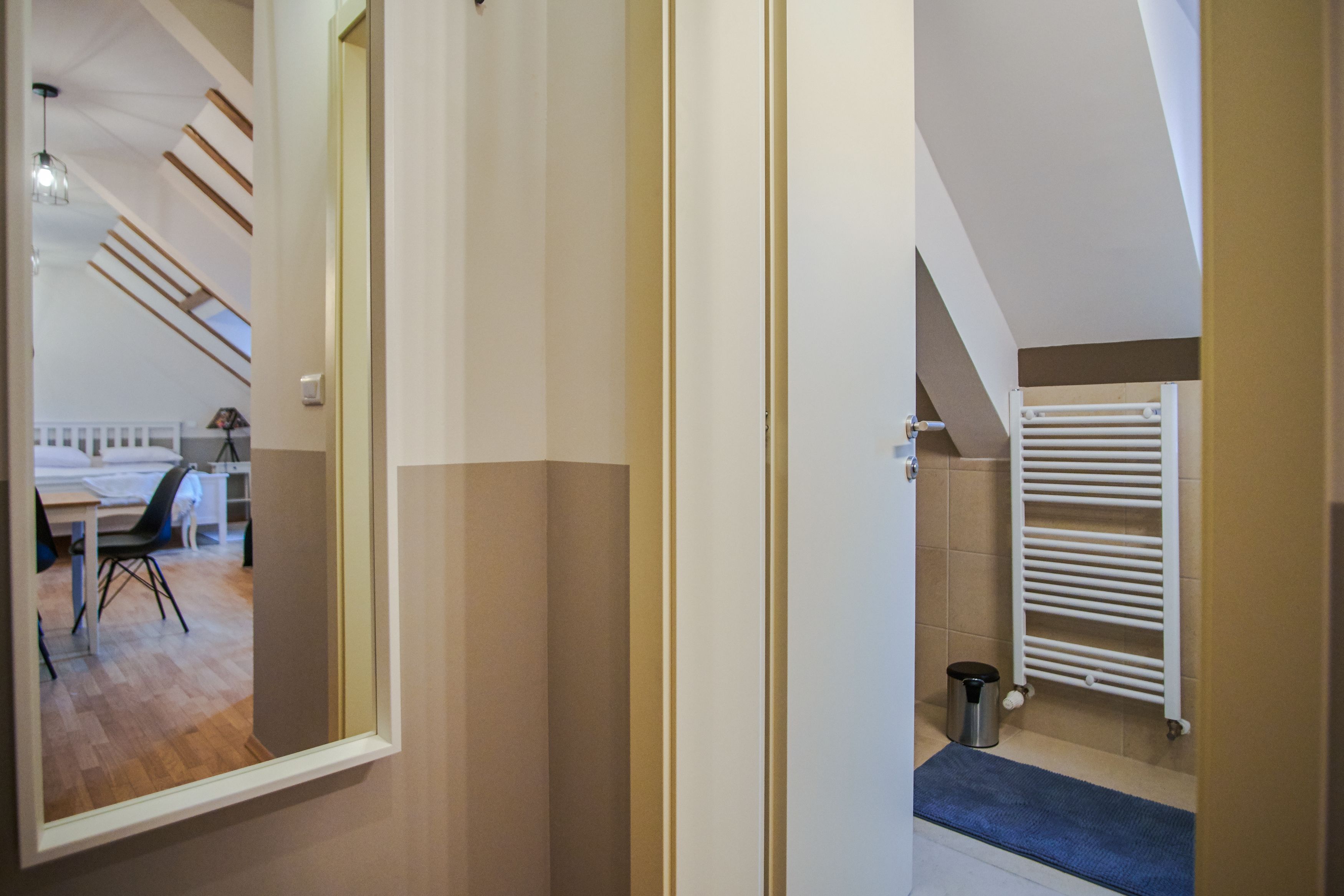A room with a bed, a desk, and a chair. There is a window, a radiator, and a trash bin.
