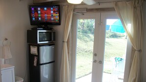 A compact kitchen with a refrigerator, microwave, and a flat-screen TV mounted on the wall. - Tiny House Vacation, Bayfront with private beach area!  On two secluded acres! (Dunmore Town)