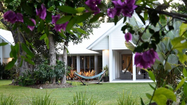 Una casa moderna con fachada blanca, una hamaca en el patio y abundante vegetación.