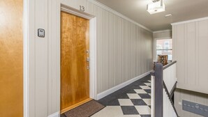 Un pasillo con una puerta de madera marcada con el número 13, piso a cuadros y una escalera con barandilla.