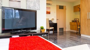 Un saló modern amb un gran televisor de pantalla plana, una catifa vermella i una zona de dinar amb una cadira i taula.