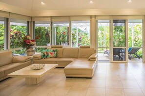 Amplia sala de estar con un sofá seccional color beige, una mesa de centro y vistas a exuberante vegetación a través de grandes ventanales.